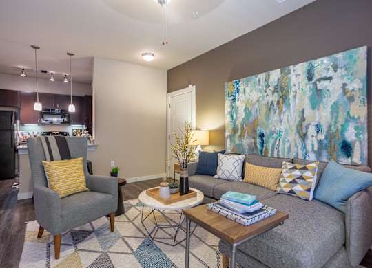 A living room with a grey couch, a yellow pillow, a grey armchair, a coffee table, and a painting on the wall.