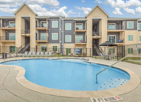 Pool with an apartment building in background and blue sky with clouds