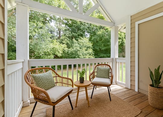 A white chair with a green pillow sits on a porch.