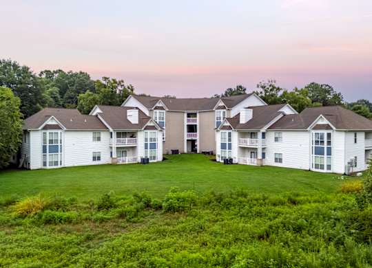 A large white building with multiple windows and balconies is surrounded by greenery.