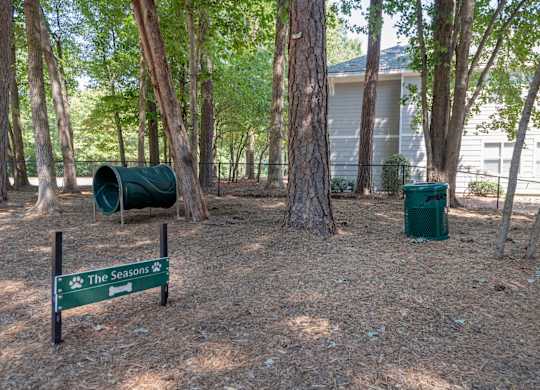 Bark park surrounded by trees with dog exercise equipment at  Seasons at Umstead apartments in Raleigh