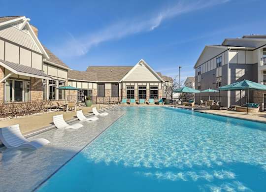 a swimming pool with chairs and umbrellas in front of a building with apartments