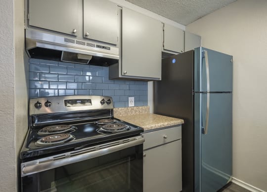 1 Bedroom Apartments in Duluth, GA - The Eclipse - Kitchen with Stainless Steel Appliances, Granite Countertops, Light Grey Cabinetry, Tile Backsplash, and Designer Wood Look Plank Flooring