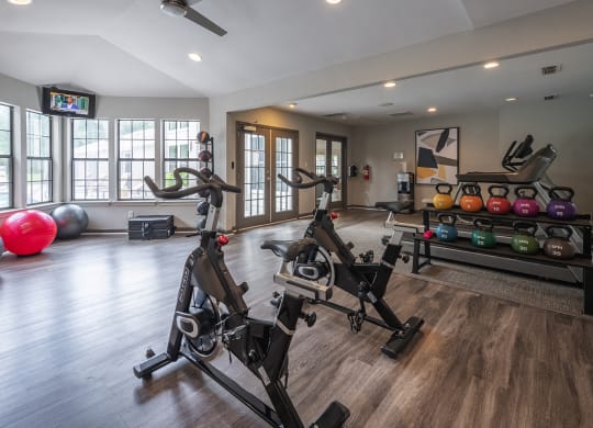 a modern apartment complex gym with weights and cardio equipment and windows