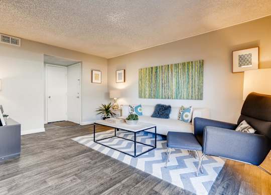 A living room with a black and white chevron rug, a black leather chair, a white couch with blue and white pillows, a wooden coffee table, and a white wall with two framed pictures at The Ranch at Bea