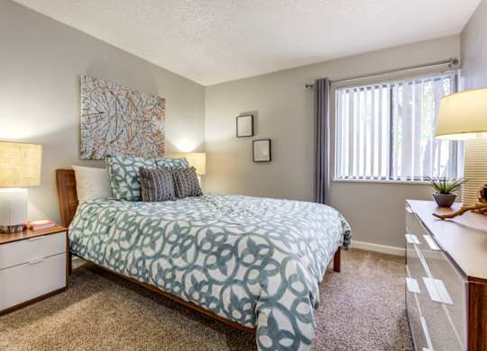 A bedroom with a bed, nightstand, and window at The Ranch at Bear Creek Apartments, Lakewood, CO