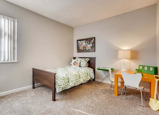 A bedroom with a bed, chair, and a painting on the wall at The Ranch at Bear Creek Apartments, Colorado