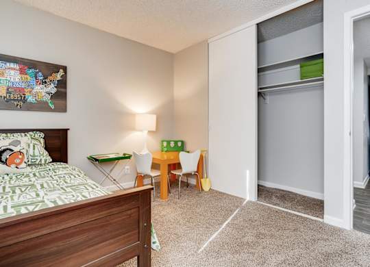 A bedroom with a bed, a table and chairs, and a refrigerator in the corner at The Ranch at Bear Creek Apartments, Lakewood, CO
