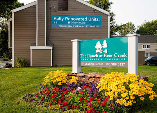 A sign for The Ranch at Bear Creek Apartments & Townhomes is displayed in front of a building.