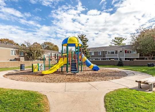 A playground with a yellow and blue slide in the middle of a grassy area at The Ranch at Bear Creek Apartments, Lakewood, CO