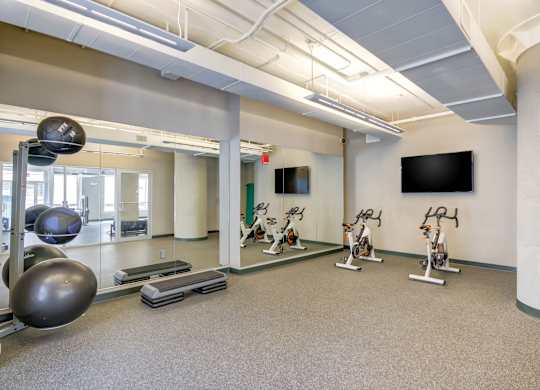 A gym with a mirror, exercise bikes, and a television.