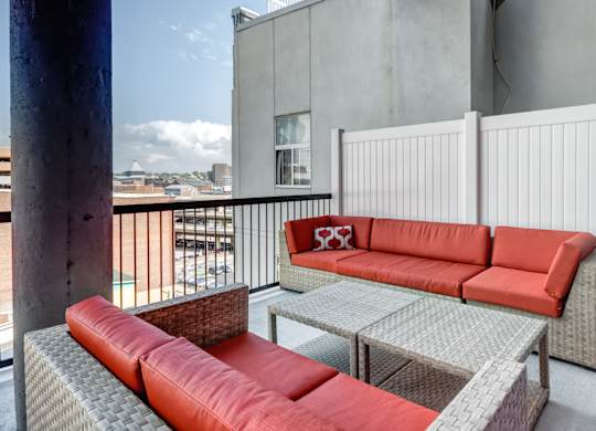 A patio with a red couch and a table with a glass top.