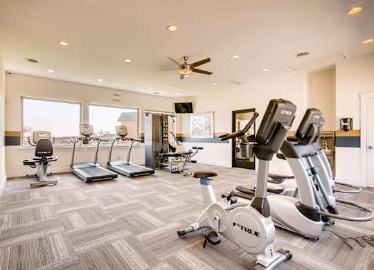 A gym with a variety of exercise equipment including treadmills, stationary bikes, and elliptical machines at Mountain Vista Apartments, Lakewood, 80228