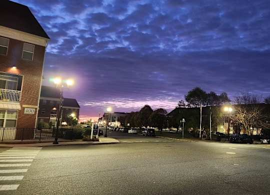 A street view of a parking lot at dusk with street lights on.
