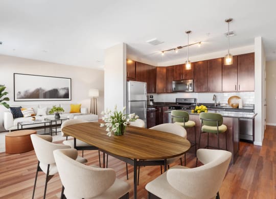 a living and dining room area with a kitchen in the background and a large table in the at West 130, West Hempstead New York