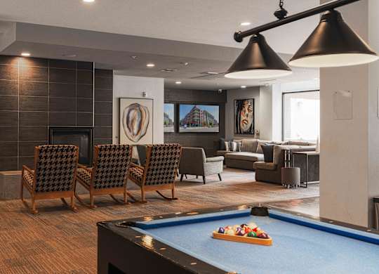 A pool table with a blue cloth and a pool game set up in a room with a fireplace and a couch at Regatta Sloans Lake Apartments, Colorado, 80204