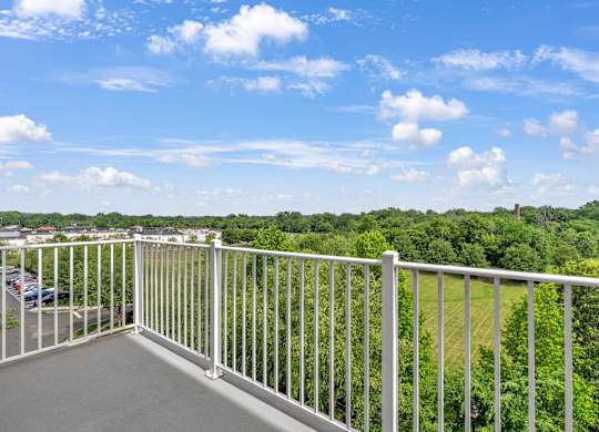 A balcony with a white railing overlooks a green landscape.