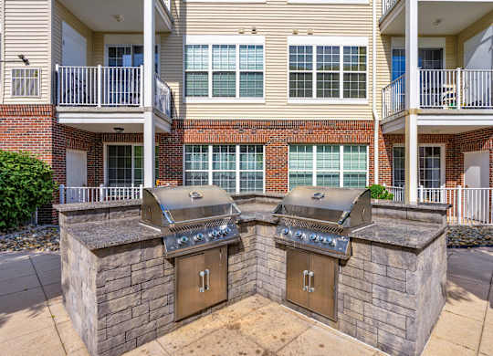 Two outdoor BBQs are built into the side of a brick building.