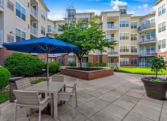 A patio with a table and chairs under an umbrella with apartment buildings in the background.