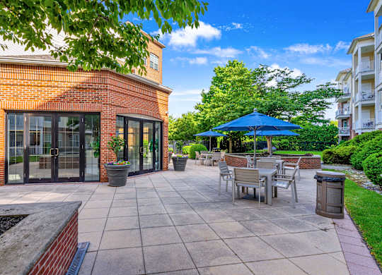 A patio with a table and chairs is surrounded by a brick building and trees.