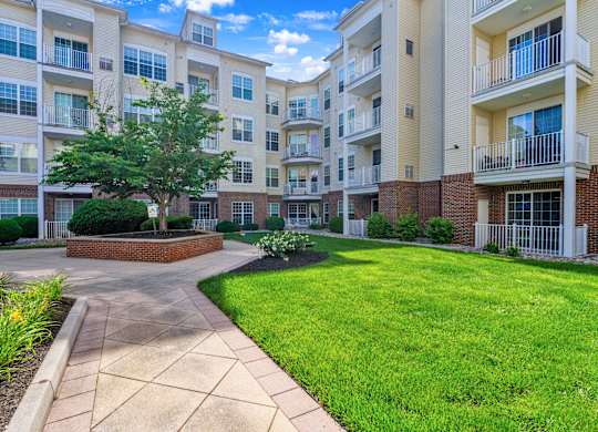 A sunny day at a brick apartment complex with a walkway and green grass.