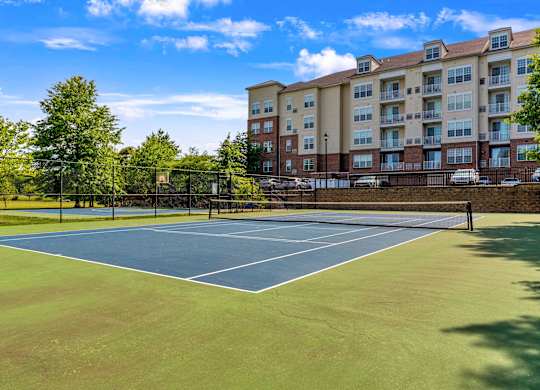 A tennis court is surrounded by a fence and apartment buildings.