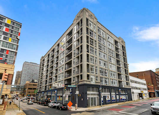 A large, multi-story building with a flat roof is situated on a busy street corner.