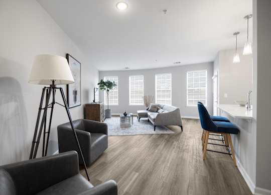 A well-lit living room with a grey sofa, a black chair, and a wooden floor.