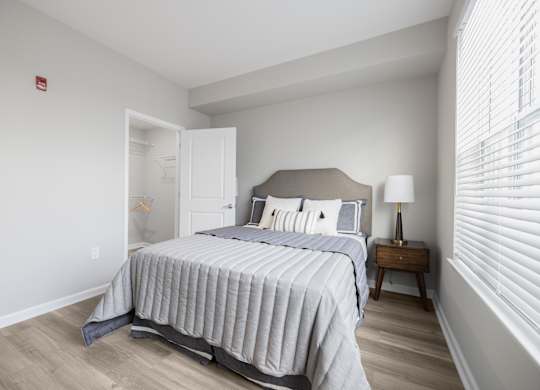 A bedroom with a bed, nightstand, and window with blinds.