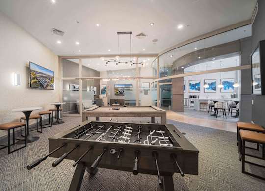 A room with a foosball table in the center and a bar area to the left at Harbor Pointe Apartments, Bayonne 07002