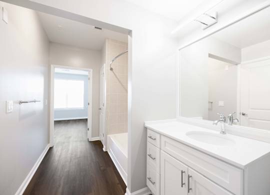 A white bathroom with a sink, mirror, and wooden floor.