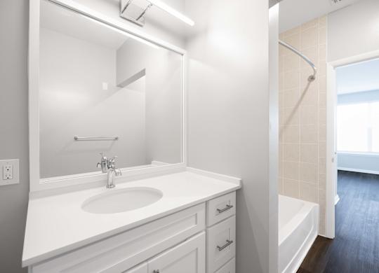 A white bathroom with a sink, mirror, and bathtub.