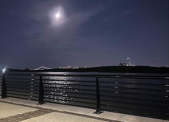 A bright light is shining in the sky over a body of water.