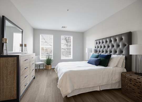 A bedroom with a large bed, a wooden dresser, and a mirror at Harbor Pointe Apartments, Bayonne, NJ, 07002