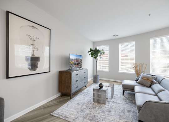 A living room with a grey sofa, a grey rug, a wooden cabinet, a side table, a potted plant, and a framed picture on the wall at Harbor Pointe Apartments, New Jersey