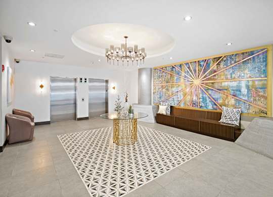 A large, modern living room with a chandelier, a sofa, a coffee table, and a large, colorful mural on the wall.