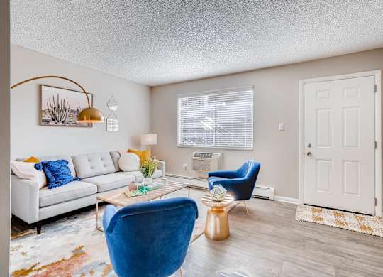 A living room with a white couch, blue chair, and a coffee table at Mountain Vista Apartments, Lakewood, CO, 80228