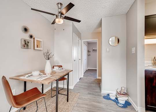 A dining room with a brown chair and a table with a vase of flowers on it at Mountain Vista Apartments, Lakewood