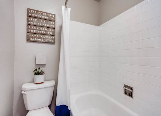 A white toilet sits next to a white bathtub in a bathroom at Mountain Vista Apartments, Colorado