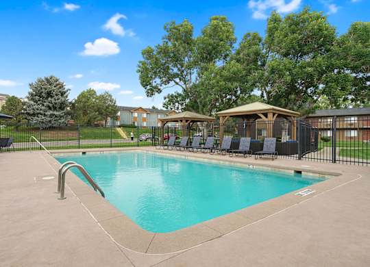 A swimming pool surrounded by a black fence and trees at Mountain Vista Apartments, Lakewood, 80228