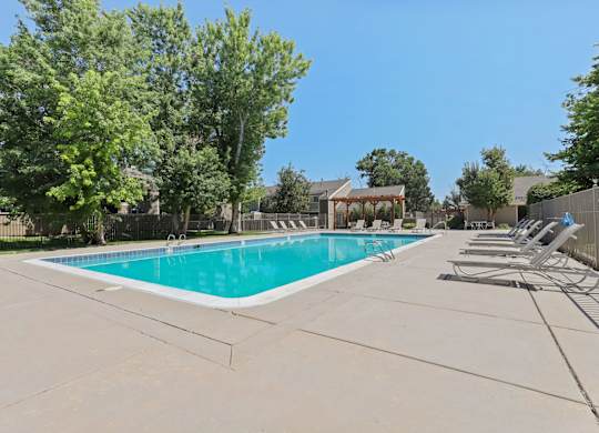 A large swimming pool surrounded by trees and lounge chairs at The Ranch at Bear Creek Apartments, Lakewood