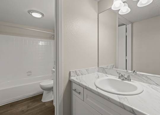 A white bathroom with a toilet, sink, and mirror at The Ranch at Bear Creek Apartments, Lakewood, CO, 80227