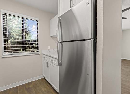 A stainless steel refrigerator in a kitchen with wooden flooring and a window with blinds at The Ranch at Bear Creek Apartments, Lakewood, Colorado