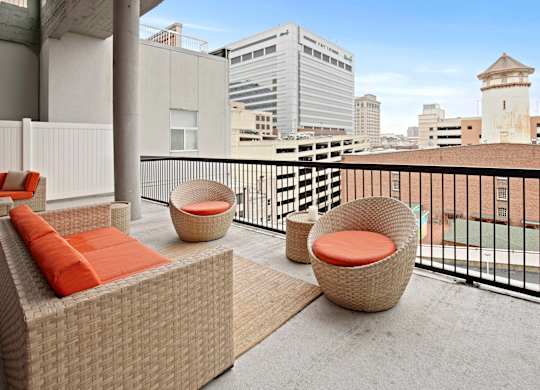 A balcony with a couch, chair and table with orange cushions.