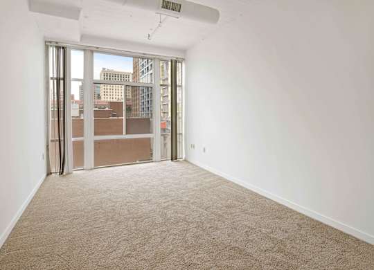 A room with a carpet floor and a window with a view of the city.