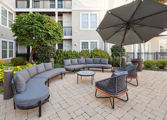 Outdoor patio with a grey couch, a black chair and a black umbrella at West 130, West Hempstead, New York 