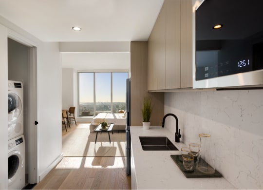 a kitchen with a sink and a dishwasher and a living room with a window at The Paxton, Brooklyn, NY 11201