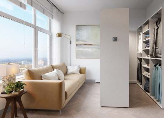 A room with a tan couch, a wooden table, and a large window overlooking the city.