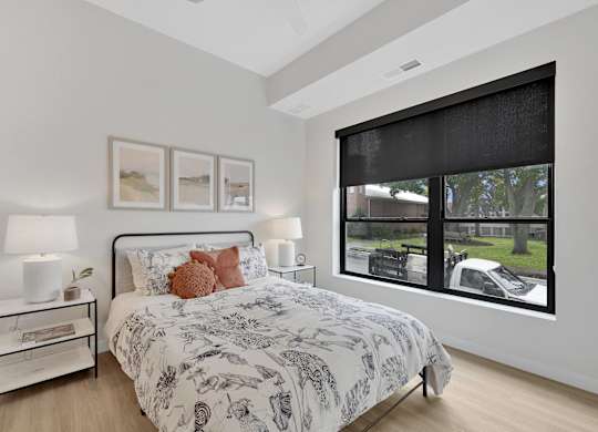 A bedroom with a large bed and a window showing a car and trees outside.