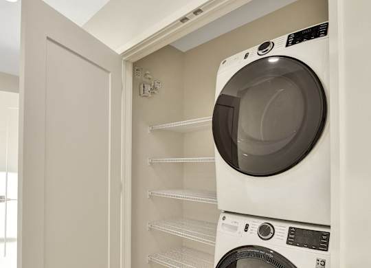 A white washing machine is in a small space between a wall and a shelf.